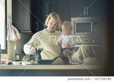 Happy mother and little infant baby boy together making pancakes for breakfast in domestic kitchen. Family, lifestyle, domestic life, food, healthy eating and people concept 101798586