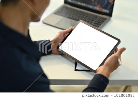 Cropped view of young businessman sitting at white office desk and using digital tablet. Blank screen for advertise text 101801085