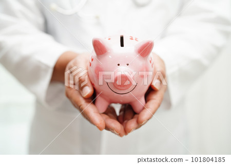 Asian woman doctor holding piggy bank, cost of treatment or education concept. Asian woman doctor holding piggy bank, cost of treatment or education concept. 101804185