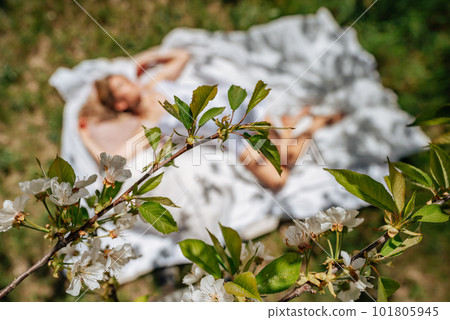 woman sleeps on a white bed in the fresh spring grass in the garden. Dressed in a blue nightgown. woman sleeps on a white bed in the fresh spring grass in the garden. Dressed in a blue nightgown. 101805945