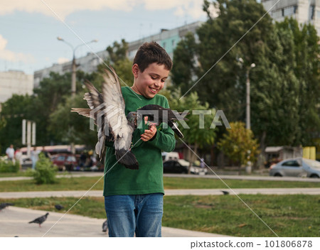 Happy positive smiling multi-ethnic teenage boy feeding pigeons on the square on a sunny spring day. The concept of love, care and compassion for wild animals. People. Nature. Lifestyle 101806878