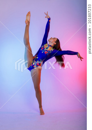 A girl gymnast in a swimsuit does tricks on a white and dark background. Front view A girl gymnast in a swimsuit does tricks on a white and dark background. Front view 101807233