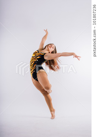 A girl gymnast in a swimsuit does tricks on a white and dark background. Front view A girl gymnast in a swimsuit does tricks on a white and dark background. Front view 101807236