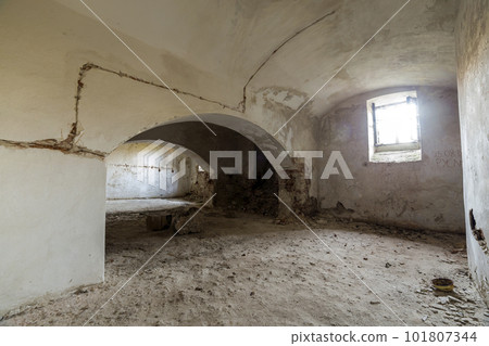 Old forsaken empty basement room of ancient building or palace with cracked plastered brick walls, low arched ceiling, small windows with iron bars and dirty floor. 101807344