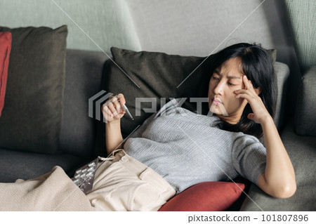 Sick asian woman reading clinical thermometer while cough on a sofa bed at home. 101807896