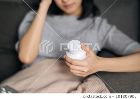 Asian woman with cold and flu reading instructions on medicine bottle 101807903