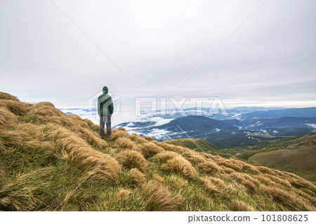 Male climber tourist standing on grassy hill slope on green mountains with white puffy clouds and blue sky copy space background. 101808625