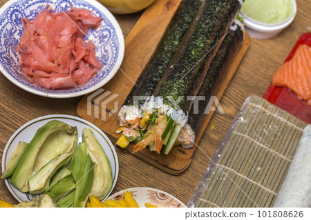 Making sushi and rolls at home. Plates with ingredients for traditional Japanese food and sushi rolls on wooden board on kitchen table, view from above. 101808626