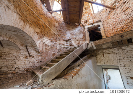 Large spacious forsaken empty basement room of ancient building or palace with cracked plastered brick walls, small windows, dirty floor and wooden staircase ladder. 101808672