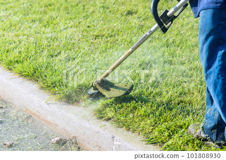 Municipal worker lawn mower mowing fresh green grass near road with his hand lawn mower trimmer 101808930