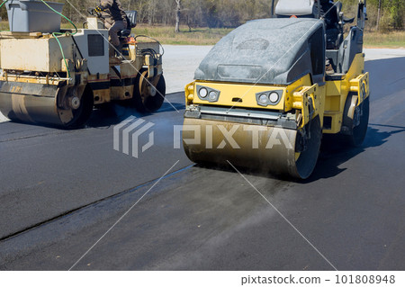 Worker operating vibratory road roller compactor process machine laying new asphalt on construction site 101808948