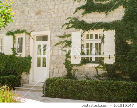 Cozy white stone house covered with ivy plant in village on sunny day Cozy white stone house covered with ivy plant in village on sunny day 101810147
