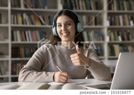 Student girl showing thumbs up seated at desk in library Student girl showing thumbs up seated at desk in library 101816977