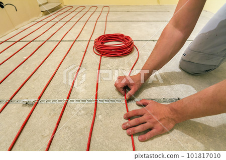 Electrician installing heating red electrical cable wire on cement floor in unfinished room. Renovation and construction, comfortable warm home concept. Electrician installing heating red electrical cable wire on cement floor in unfinished room. Renovation and construction, comfortable warm home concept. 101817010