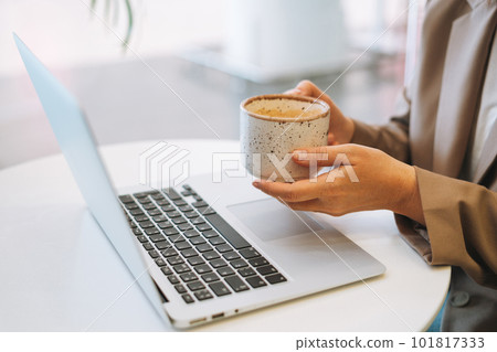 Business woman with long hair in stylish beige suit working at laptop drinking coffee on table 101817333