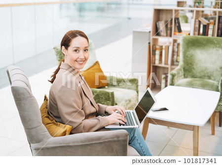 Adult smiling brunette business woman with long hair in beige suit and jeans working on laptop Adult smiling brunette business woman with long hair in beige suit and jeans working on laptop 101817341