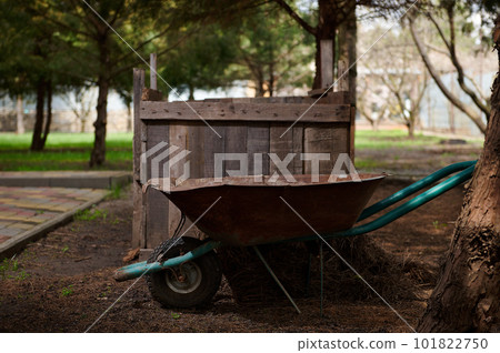 Still life with wheelbarrow standing near a compost pit in a garden plot. Agriculture. Eco farming. Gardening. Agricultural hobby. Sustainable resources. Sustainability. Zero waste concept. Composting Still life with wheelbarrow standing near a compost pit in a garden plot. Agriculture. Eco farming. Gardening. Agricultural hobby. Sustainable resources. Sustainability. Zero waste concept. Composting 101822750