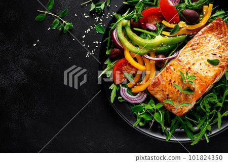 Salmon fillet grilled and fresh vegetable green salad of arugula with tomatoes, olives and bell pepper on black background, healthy food, mediterranean diet, top view Salmon fillet grilled and fresh vegetable green salad of arugula with tomatoes, olives and bell pepper on black background, healthy food, mediterranean diet, top view 101824350