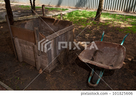Still life with a wooden compost bin and wheelbarrow. Close up DIY compost bin to improve the fertility and soil structure in the garden. Zero waste concept. Organic farming. Sustainability Still life with a wooden compost bin and wheelbarrow. Close up DIY compost bin to improve the fertility and soil structure in the garden. Zero waste concept. Organic farming. Sustainability 101825606