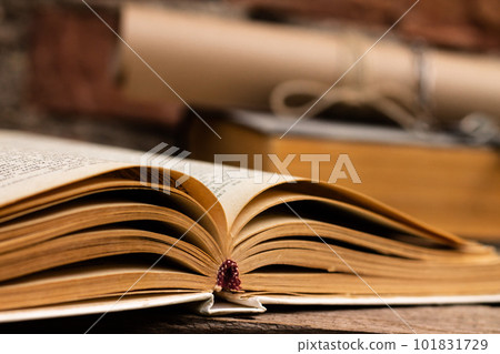 Old books with a scroll and key on a rustic wooden surface on a brick wall background. 101831729