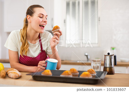 Woman in apron tasting freshly baked sweet cupcakes in kitchen 101833607