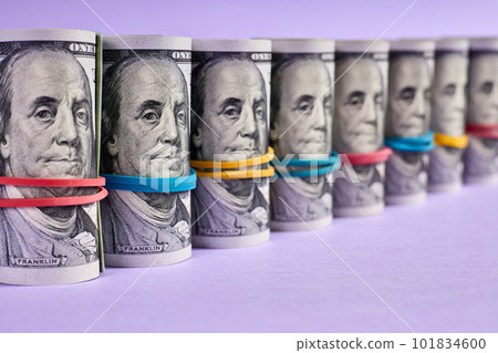 A row of rolled hundred dollar bills with rubber bands on purple background A row of rolled hundred dollar bills with rubber bands on purple background 101834600
