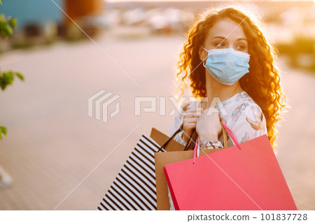 Woman in shopping. Young girl in protective sterile medical mask on her face with shopping bags. Woman in shopping. Young girl in protective sterile medical mask on her face with shopping bags. 101837728