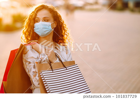 Woman in shopping. Young girl in protective sterile medical mask on her face with shopping bags. Woman in shopping. Young girl in protective sterile medical mask on her face with shopping bags. 101837729