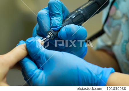 A manicurist in blue gloves makes a manicure with a device. Cuticle treatment 101839988