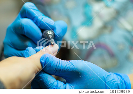A manicurist in blue gloves makes a manicure with a device. Cuticle treatment 101839989