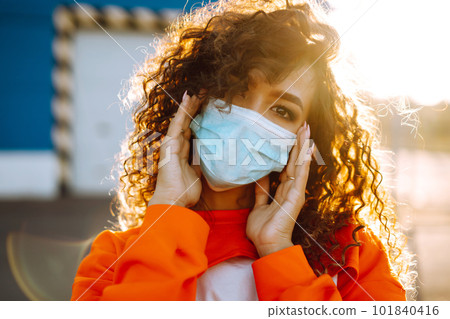 Young woman with medical face mask at sunset. Curly woman posing during quarantine of coronavirus pandemic. 101840416