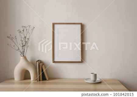Empty wooden picture frame mockup hanging on beige wall background. Boho shaped vase, dry flowers on table. Cup of coffee, old books. Working space, home office. Art, poster display. Modern interior. Empty wooden picture frame mockup hanging on beige wall background. Boho shaped vase, dry flowers on table. Cup of coffee, old books. Working space, home office. Art, poster display. Modern interior. 101842015