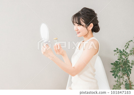 Smiling Asian woman holding a bottle of medicine/supplements while looking in the mirror 101847183