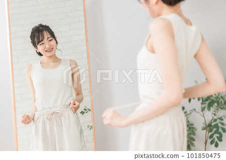 一位面帶微笑的亞洲女性在鏡子前測量自己的腰圍(節食、收縮、縮小、三種尺寸) 一位面帶微笑的亞洲女性在鏡子前測量自己的腰圍(節食、收縮、縮小、三種尺寸) 101850475