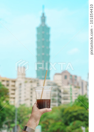 Woman hand holding a glass of ice coffee against Taipei city background 101854410
