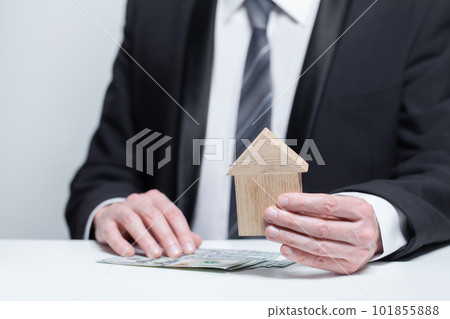 Us money dollars and wooden house above it in businesman hands on white background. Byuing property 101855888