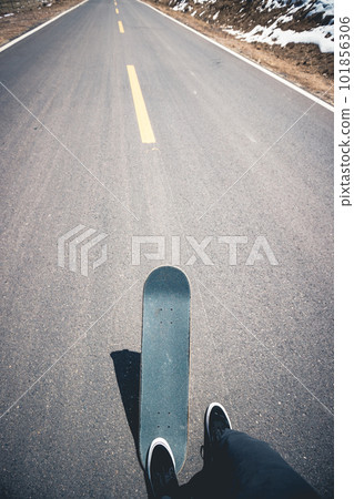 Asian woman skateboarder skateboarding on snowy country road 101856306