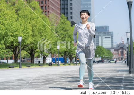 A middle-aged woman jogging in a park in an office district A middle-aged woman jogging in a park in an office district 101856392