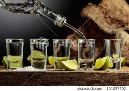 Tequila is poured from a bottle into a glass. Tequila is poured from a bottle into a glass. 101857302