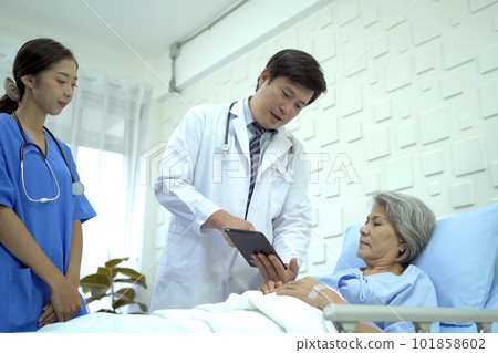 Senior Asian female patient resting on the medical bed in hospital and talking to her son. Son visiting and talking to his mother who staying in recovery ward. Doctor talking to asian elder patient. 101858602