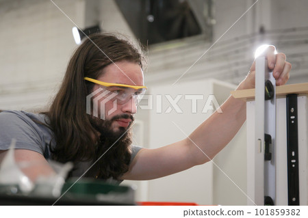 Professional carpenters using a ruler and spirit level to measures a wood panel. Professional carpenter measuring a wood plank. Professional carpenters using a ruler and spirit level to measures a wood panel. Professional carpenter measuring a wood plank. 101859382