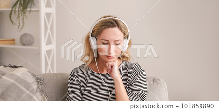 Music healing. Upset woman. Sound recovery. Depressed lady listening favorite melody on headphones sitting in light room interior. Music healing. Upset woman. Sound recovery. Depressed lady listening favorite melody on headphones sitting in light room interior. 101859890