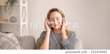 Pleasant music. Inspired woman. Stereo sound. Happy relaxed lady listening favorite song on headphones closing eyes in light room interior. Pleasant music. Inspired woman. Stereo sound. Happy relaxed lady listening favorite song on headphones closing eyes in light room interior. 101859891