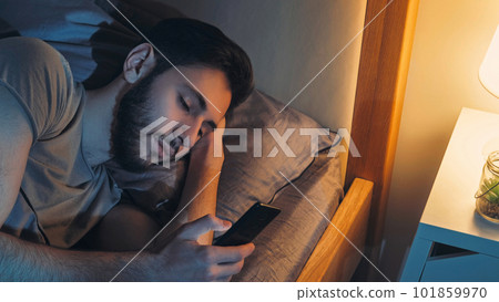 Night chat. Gadget insomnia. Online communication. Relaxed man texting reading message using smartphone in bed in home bedroom. Night chat. Gadget insomnia. Online communication. Relaxed man texting reading message using smartphone in bed in home bedroom. 101859970