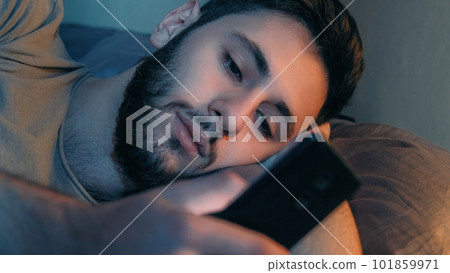 Phone night. Mobile chat. Internet insomnia. Bored tired restless guy using gadget texting message scrolling feed in bed late in dark home bedroom. 101859971