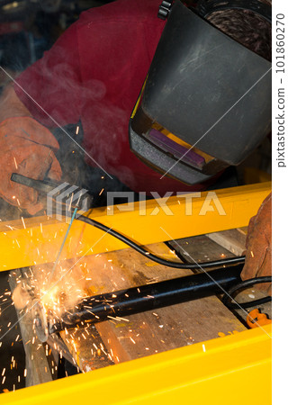 Welder welding a metal part in an industrial environment, wearing standard protection equipment 101860270