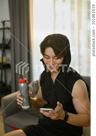 Sport man using smartphone on couch in domestic home. 101861019