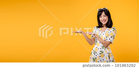 Portrait beautiful young asian woman wearing springtime dress and pointing to copy space for advertising isolated on yellow background. Summertime advertising banner concept. 101863202