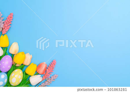 Happy Easter holiday greeting card design concept. Colorful Easter Eggs and spring flowers on blue background. Flat lay, top view, copy space. 101863281