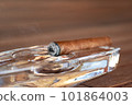 Burning Cuban cigar in a glass ashtray 101864003